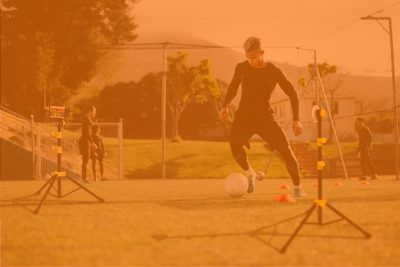 Young soccer player training with Tendo Sprint System by Tendo Sport to improve his speed in football field with team in background in orange