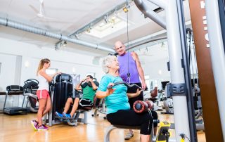 Senior woman doing back training with Tendo Unit by Tendo Sport and trainer in gym