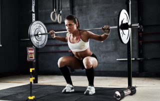 Woman athlete weight training with Tendo Unit by Tendo Sport while performing squats in a gym and measuring her athletic performance