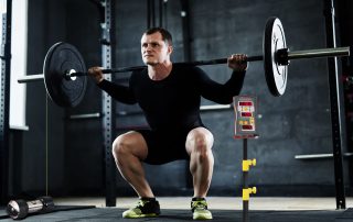 Strong young man with weight training in gym using Tendo Unit power analyser by Tendo Sport to measure his power and velocity of each rep