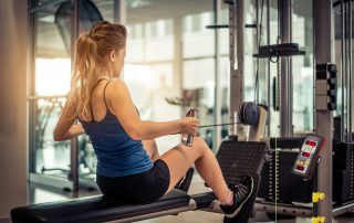 Woman athlete training her back and shoulder with weight machine in a gym with Tendo unit by Tendo Sport being attached to the weight stack and Tendo microcomputer unit with performance results being in her sight