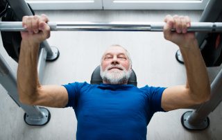 Senior man in sports clothing in gym working out with weights, bench pressing while using by Tendo Sport products.